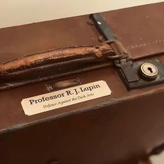 a brown suitcase with a label on it that says professor r i lupin, defaced against the dark side