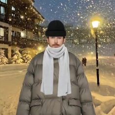 a man standing in the snow wearing a hat and scarf