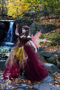 a woman dressed as a fairy holding an umbrella in front of a waterfall and fall foliage