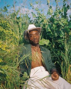 a person sitting in tall grass with a hat on their head and one hand resting on the ground