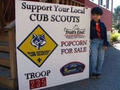 a young boy standing next to a sign advertising cub scouts