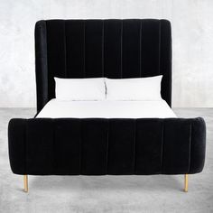 a bed with white pillows and black headboard on concrete floored area, next to wall