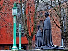 a statue in front of a red brick building with a clock tower and lamp post