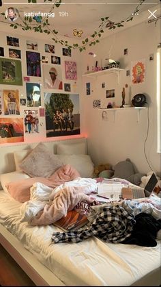 an unmade bed in a bedroom with pictures on the wall and clothes hanging from the ceiling