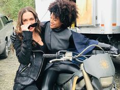 two women are sitting on a motorcycle and one is holding her hand up to her face