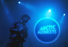 a man standing in front of a microphone on stage with the arctic monkeys logo behind him