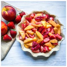 a bowl filled with fruit next to two apples and strawberries on a cutting board