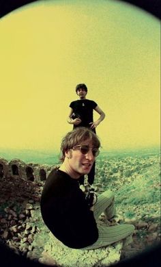 two young men are sitting on top of a rock wall and one is holding a camera