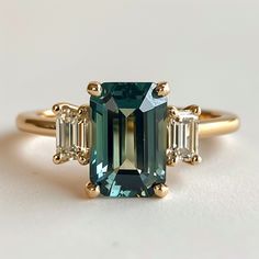 an emerald and diamond ring with three baguets on the side, set in yellow gold