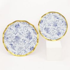 two blue and white plates sitting next to each other on top of a stand in front of a white wall