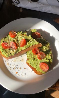 an avocado and tomato toast on a white plate