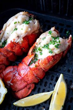 two cooked lobsters on a grill with lemon wedges and parmesan cheese