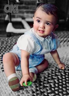 a small child sitting on the ground playing with a green ball and smiling at the camera