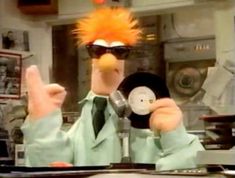 an orange haired man wearing sunglasses and holding a record in front of his face while sitting at a desk