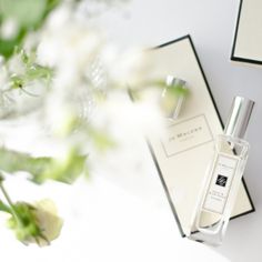 a bottle of perfume next to some flowers on a white table with two black and white boxes