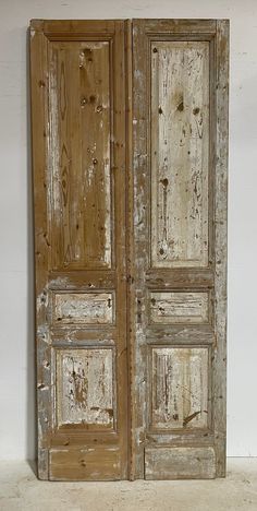 an old wooden door with peeling paint on the doors and side panels, in a white room