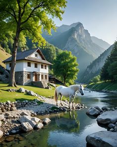 a white horse standing next to a river in front of a house with mountains behind it