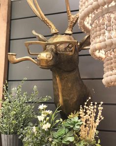 a statue of a deer with glasses on it's head next to some plants