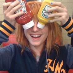 a woman holding two ketchup bottles in front of her eyes and covering her eyes with both hands