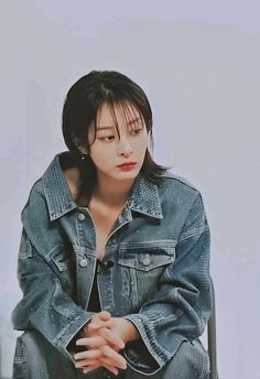 a woman sitting on top of a chair wearing a jean jacket and holding her hands together