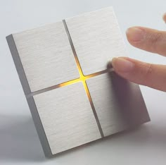 a hand is holding a piece of metal that looks like a cube with a cross on it