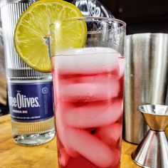 a tall glass filled with red and white liquid next to a metal shaker full of lemon wedges