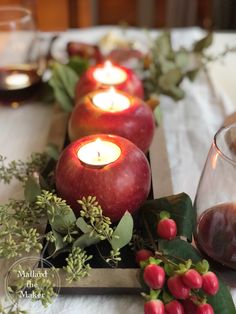 some apples are sitting on a table with candles and greenery in front of them