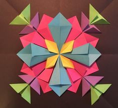 an origami flower made out of colored paper on a brown background with other folded objects