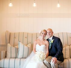 a bride and groom sitting on a couch in front of a wall with striped pillows