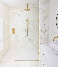 a white bathroom with gold fixtures and marble tile on the walls, along with a walk in shower