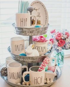 three tiered tray holding cups and dishes with words written on them, along with flowers