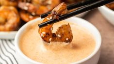 chopsticks sticking out of a bowl filled with dipping sauce and fried chicken wings