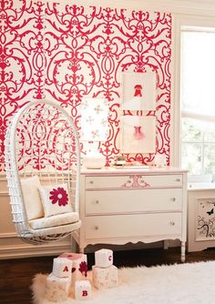 a white chair sitting in front of a window next to a dresser and wallpaper