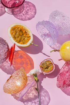 various fruits and vegetables are arranged on a pink surface with petals, leaves, and flowers