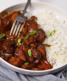 a white bowl filled with meat and rice on top of a blue cloth next to a fork