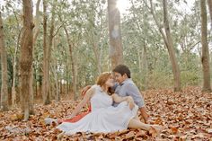 a man and woman are sitting in the leaves on the ground with trees behind them