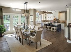 a dining room and kitchen area in a home with hardwood floors, white cabinets, and large windows