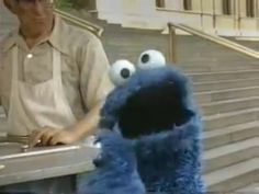 a man sitting at a table next to a sesame street cookie monster with big eyes