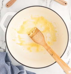 a wooden spoon in a white bowl filled with liquid and sugar next to utensils on a marble counter top