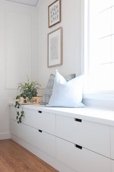 a room with white walls and wooden flooring, some plants are on the window sill