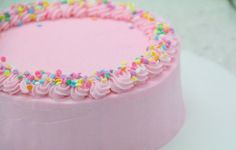 a pink frosted cake with sprinkles on it's sides and bottom