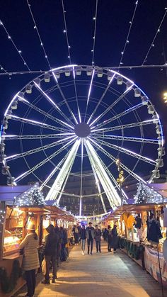 a ferris wheel is lit up at night with people walking around in the foreground