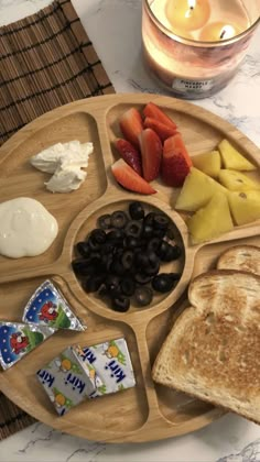 a wooden plate topped with lots of food next to a glass of milk and a candle