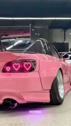 a pink car with hearts painted on it's hood and tail lights is parked in a parking garage