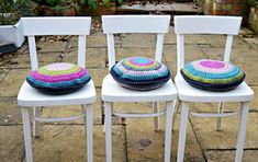 three white chairs with crocheted cushions on them