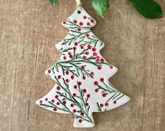 a ceramic christmas tree ornament hanging from a branch on a wooden table with leaves