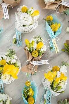 small bouquets of yellow and white flowers are arranged on a marble surface with tags