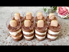 four desserts are arranged in glass cups on the table with flowers behind them and one has marshmallows sticking out of it