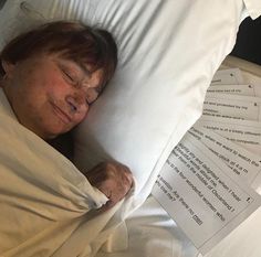 an older woman laying in bed with her head on the pillow and papers around her