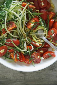 a white bowl filled with zucchini noodles and tomatoes